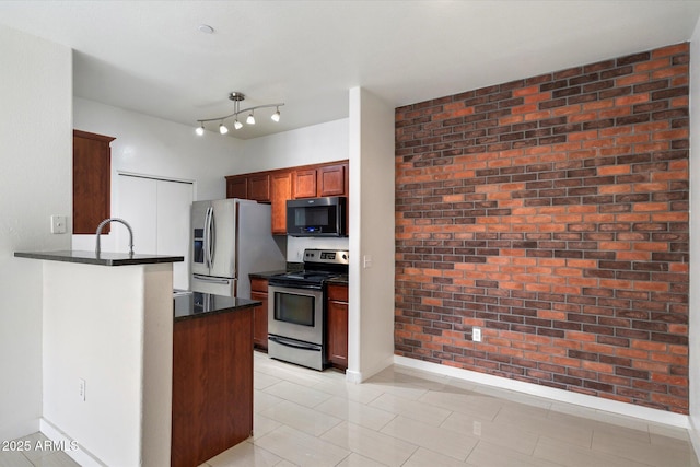 kitchen with a peninsula, rail lighting, brick wall, stainless steel appliances, and baseboards