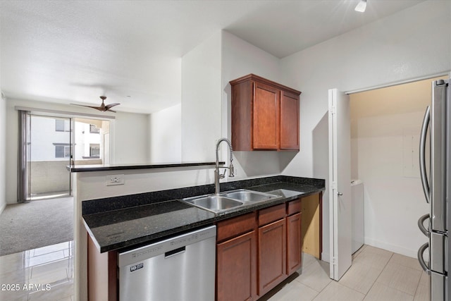 kitchen with a sink, appliances with stainless steel finishes, brown cabinets, ceiling fan, and dark stone counters