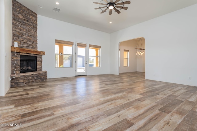 unfurnished living room with ceiling fan, a stone fireplace, and light hardwood / wood-style floors