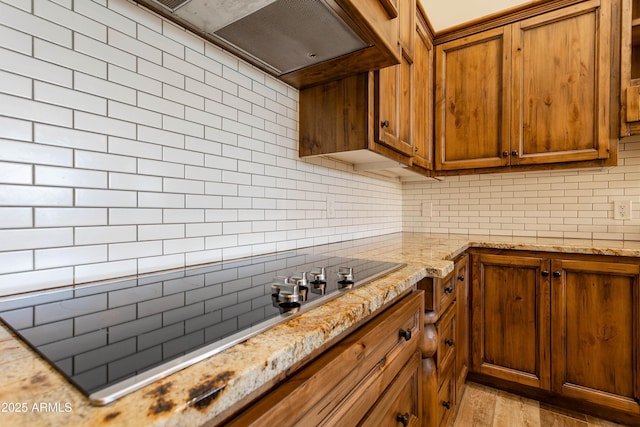 kitchen with tasteful backsplash, light stone countertops, black electric cooktop, and light hardwood / wood-style floors