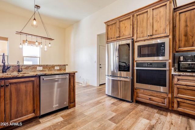 kitchen featuring sink, light wood-type flooring, appliances with stainless steel finishes, pendant lighting, and light stone countertops