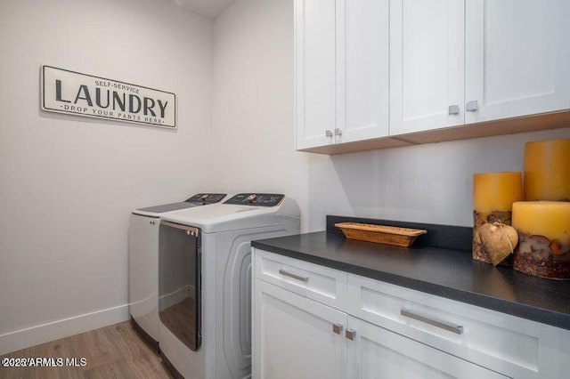 clothes washing area featuring baseboards, wood finished floors, cabinet space, and washer and dryer