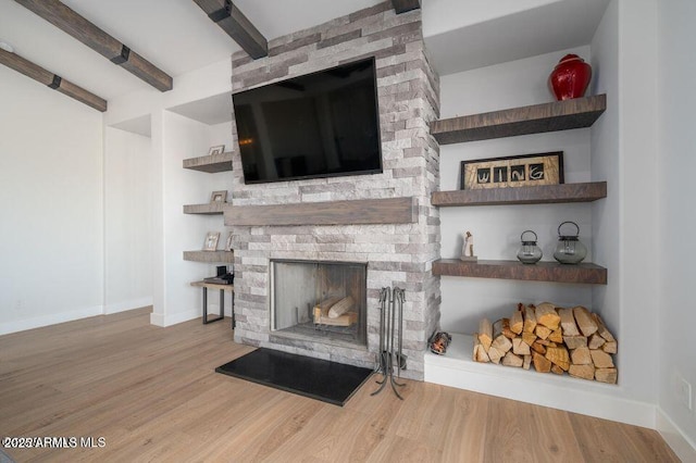 living room with beam ceiling, a large fireplace, baseboards, and wood finished floors