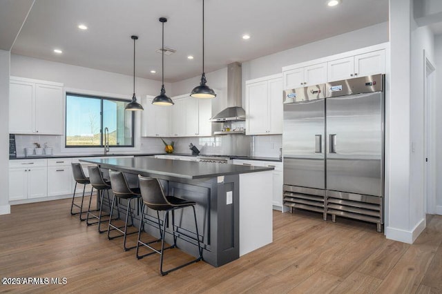 kitchen with built in fridge, a center island, dark countertops, visible vents, and wall chimney exhaust hood