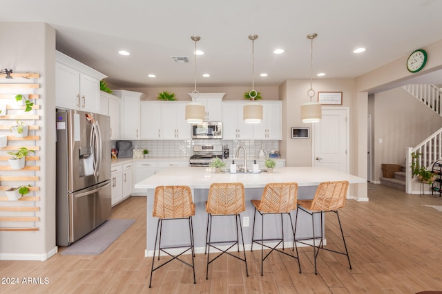 kitchen featuring white cabinets, appliances with stainless steel finishes, light wood-type flooring, and a center island with sink