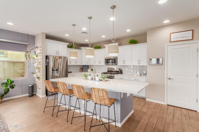 kitchen featuring stainless steel appliances, decorative light fixtures, a center island with sink, white cabinets, and light hardwood / wood-style floors