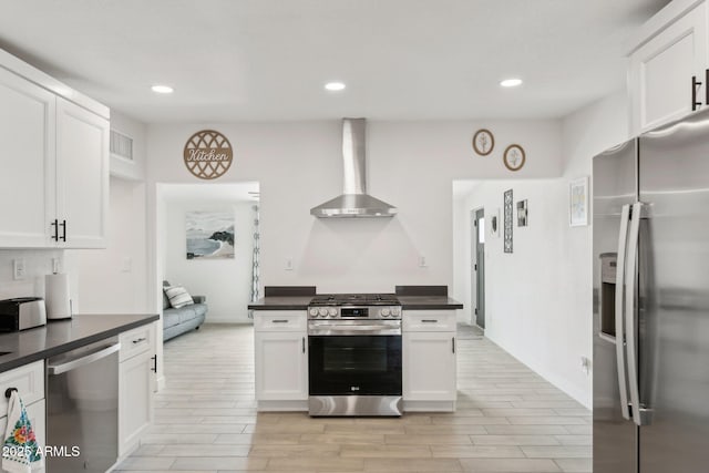 kitchen featuring stainless steel appliances, wall chimney range hood, dark countertops, white cabinetry, and recessed lighting