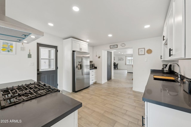 kitchen featuring appliances with stainless steel finishes, dark countertops, wall chimney range hood, a sink, and recessed lighting