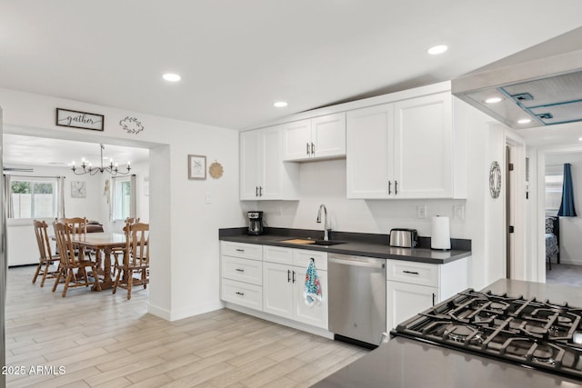 kitchen featuring dishwasher, a sink, dark countertops, white cabinets, and recessed lighting