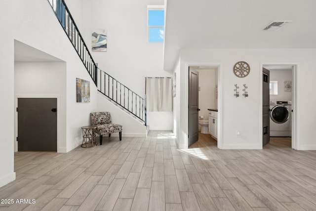 foyer featuring washer / clothes dryer, light wood-style flooring, a high ceiling, stairway, and baseboards