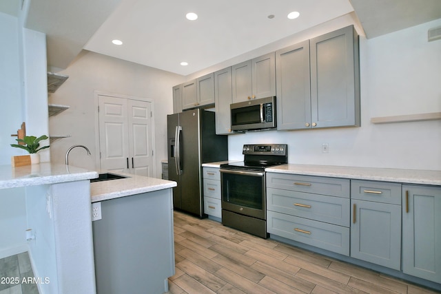 kitchen with recessed lighting, gray cabinets, appliances with stainless steel finishes, wood tiled floor, and a sink