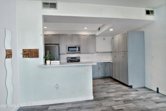 kitchen featuring visible vents, a peninsula, stainless steel appliances, light countertops, and gray cabinetry