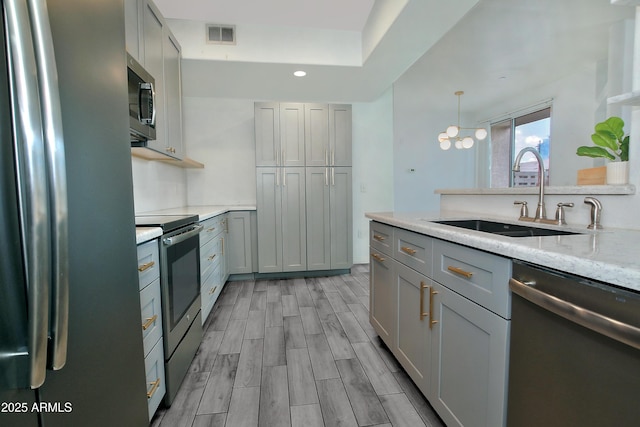 kitchen with visible vents, stainless steel appliances, gray cabinetry, wood finish floors, and a sink