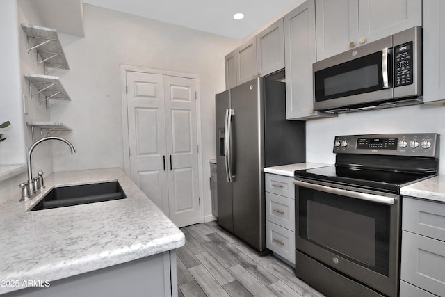 kitchen with gray cabinets, stainless steel appliances, wood finish floors, a sink, and recessed lighting