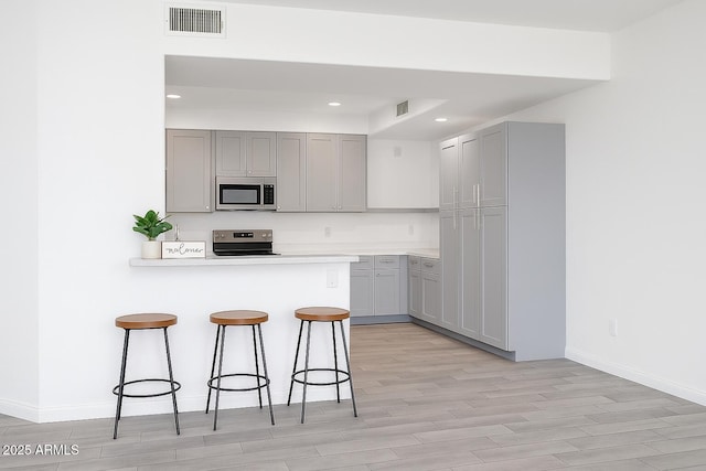 3302 N 7th St Unit 239, Phoenix, AZ 85014 - kitchen with stainless steel microwave, gray cabinets, range, a breakfast bar, and recessed lighting