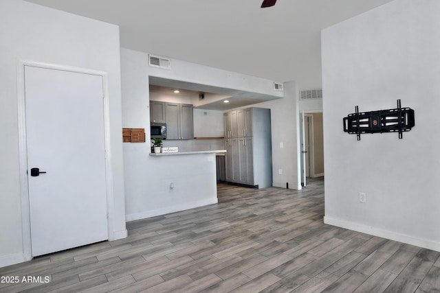 kitchen with gray cabinets, light countertops, stainless steel microwave, visible vents, and light wood-style flooring