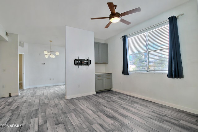 unfurnished room with visible vents, ceiling fan with notable chandelier, light wood-style flooring, and baseboards