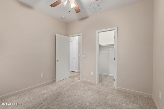 unfurnished bedroom with a walk in closet, ceiling fan, a closet, and light carpet