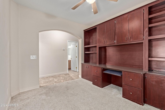 unfurnished office with ceiling fan, light colored carpet, and built in desk