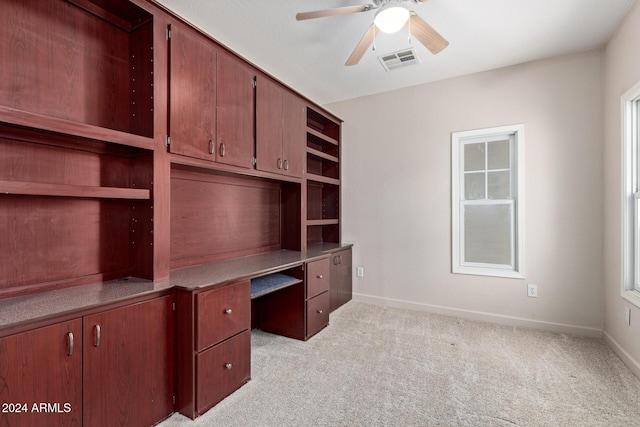 unfurnished office with light carpet, ceiling fan, and built in desk