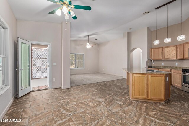 kitchen with light stone counters, stainless steel range, ceiling fan, sink, and decorative light fixtures