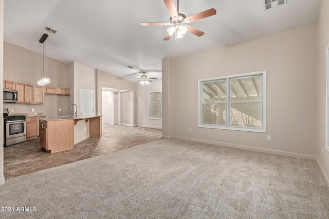 kitchen with light brown cabinetry, appliances with stainless steel finishes, pendant lighting, a center island with sink, and carpet floors