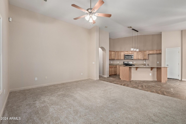 unfurnished living room with ceiling fan, carpet floors, sink, and high vaulted ceiling