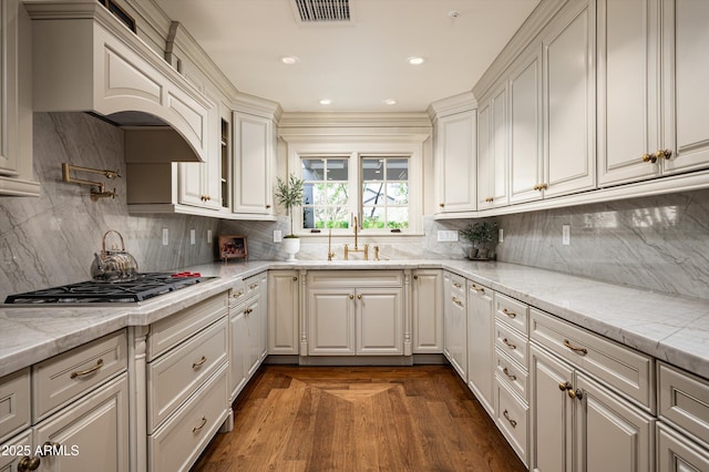 kitchen with stainless steel gas cooktop, custom range hood, decorative backsplash, a sink, and visible vents