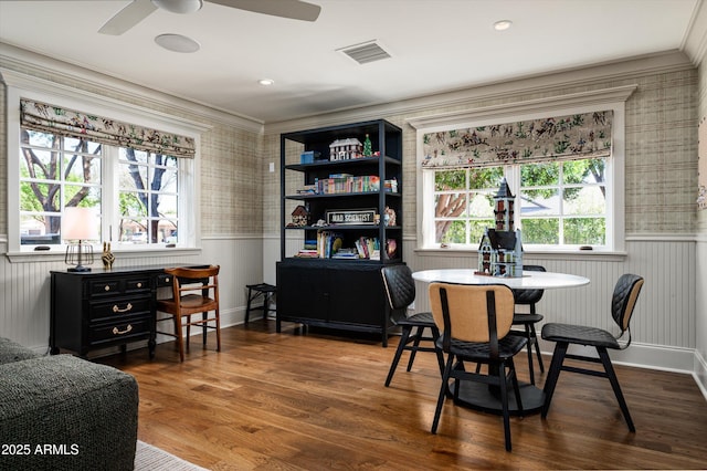 dining room with a wainscoted wall, visible vents, ceiling fan, ornamental molding, and wood finished floors