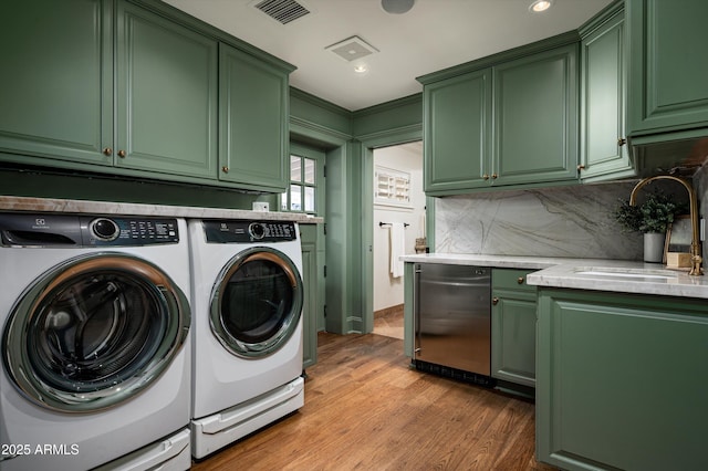 washroom with visible vents, wood finished floors, a sink, washer and dryer, and cabinet space