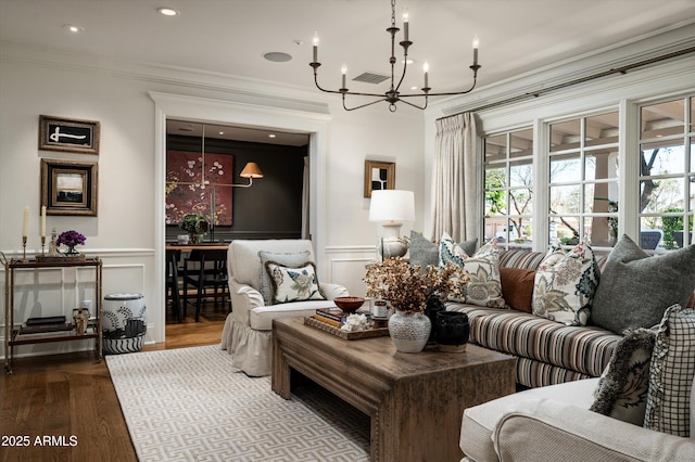 living room featuring a wainscoted wall, wood finished floors, visible vents, ornamental molding, and an inviting chandelier