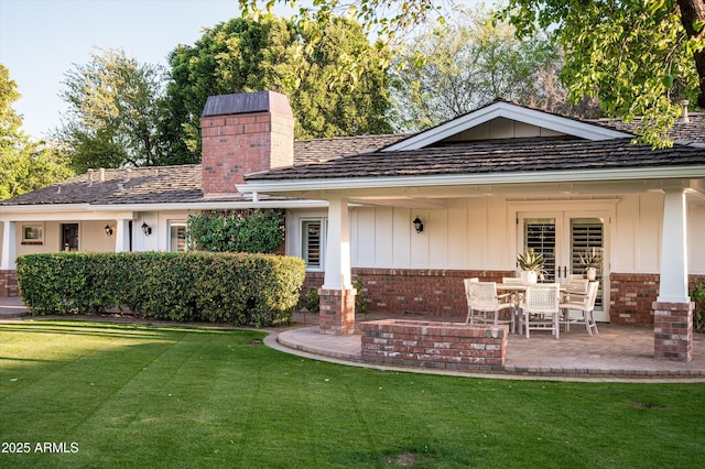 view of front of home with a patio area, a chimney, brick siding, board and batten siding, and a front lawn