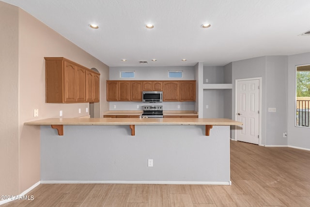 kitchen with a breakfast bar area, appliances with stainless steel finishes, light wood-type flooring, and kitchen peninsula