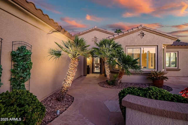 view of exterior entry featuring stucco siding, concrete driveway, and a tile roof