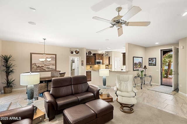 living area featuring light tile patterned floors, recessed lighting, ceiling fan with notable chandelier, and baseboards