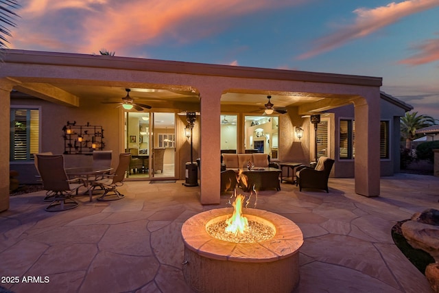 patio terrace at dusk featuring an outdoor living space with a fire pit, outdoor dining space, and ceiling fan