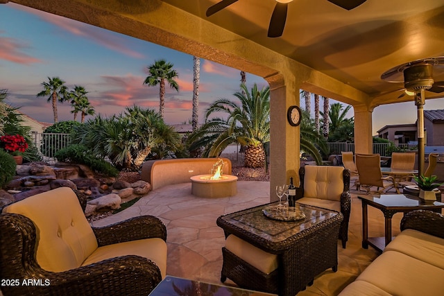 patio terrace at dusk featuring an outdoor living space with a fire pit, a fenced backyard, and a ceiling fan