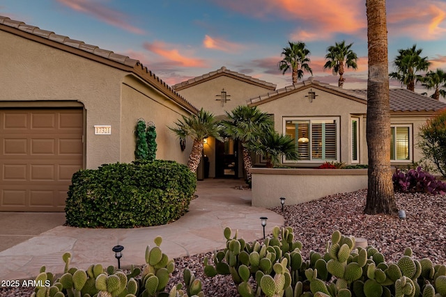 mediterranean / spanish home featuring stucco siding, an attached garage, and a tiled roof