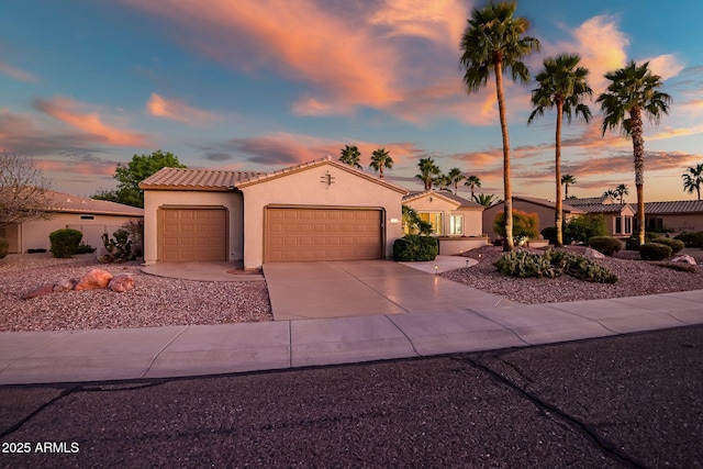 mediterranean / spanish house with a tile roof, an attached garage, driveway, and stucco siding