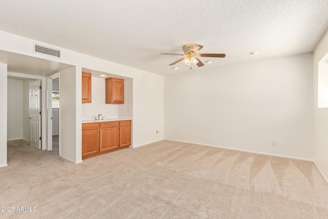 unfurnished room with a textured ceiling, visible vents, a sink, and light colored carpet