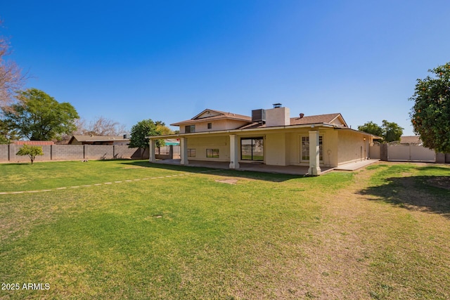 back of property featuring a patio, a chimney, stucco siding, a lawn, and a fenced backyard