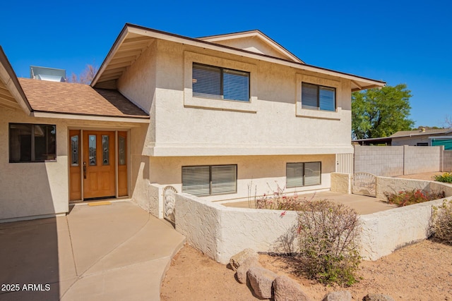 split level home with a shingled roof, fence, and stucco siding