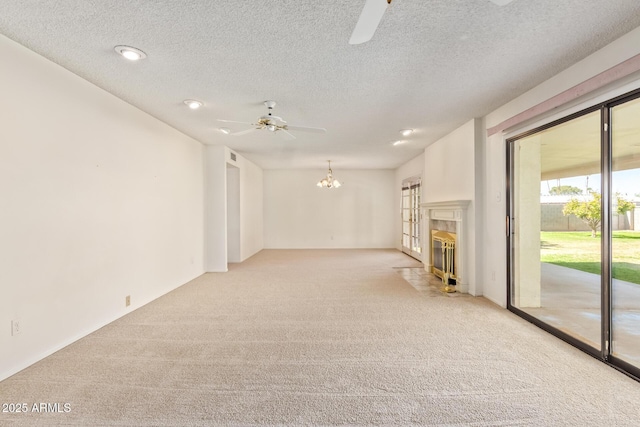 unfurnished living room with ceiling fan with notable chandelier, a textured ceiling, a fireplace with flush hearth, and light colored carpet