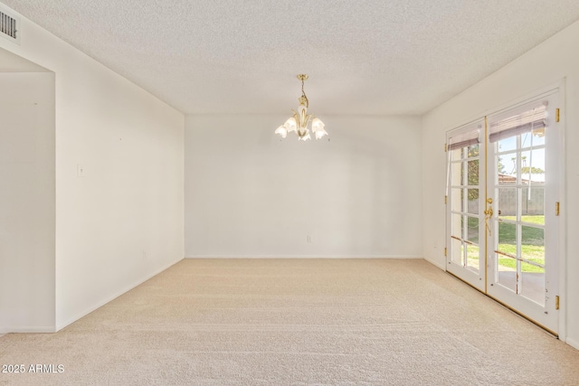 spare room featuring carpet, visible vents, a notable chandelier, and a textured ceiling