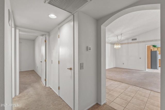 hall with a chandelier, visible vents, light colored carpet, and light tile patterned flooring
