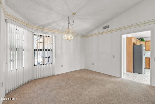 spare room with an inviting chandelier, light carpet, a textured ceiling, visible vents, and lofted ceiling
