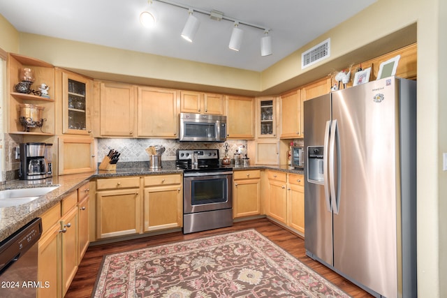 kitchen with light brown cabinets, tasteful backsplash, dark hardwood / wood-style flooring, dark stone countertops, and appliances with stainless steel finishes