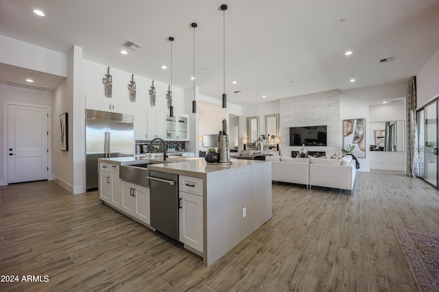 kitchen with appliances with stainless steel finishes, sink, pendant lighting, a center island with sink, and white cabinetry