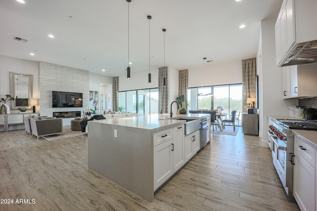 kitchen with a kitchen island with sink, white cabinets, sink, hanging light fixtures, and stainless steel appliances