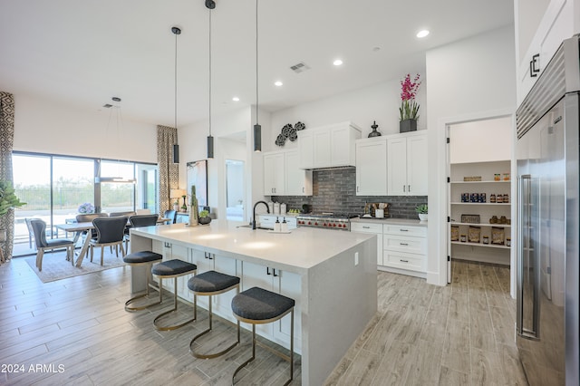 kitchen featuring pendant lighting, a breakfast bar, stainless steel built in fridge, an island with sink, and white cabinetry